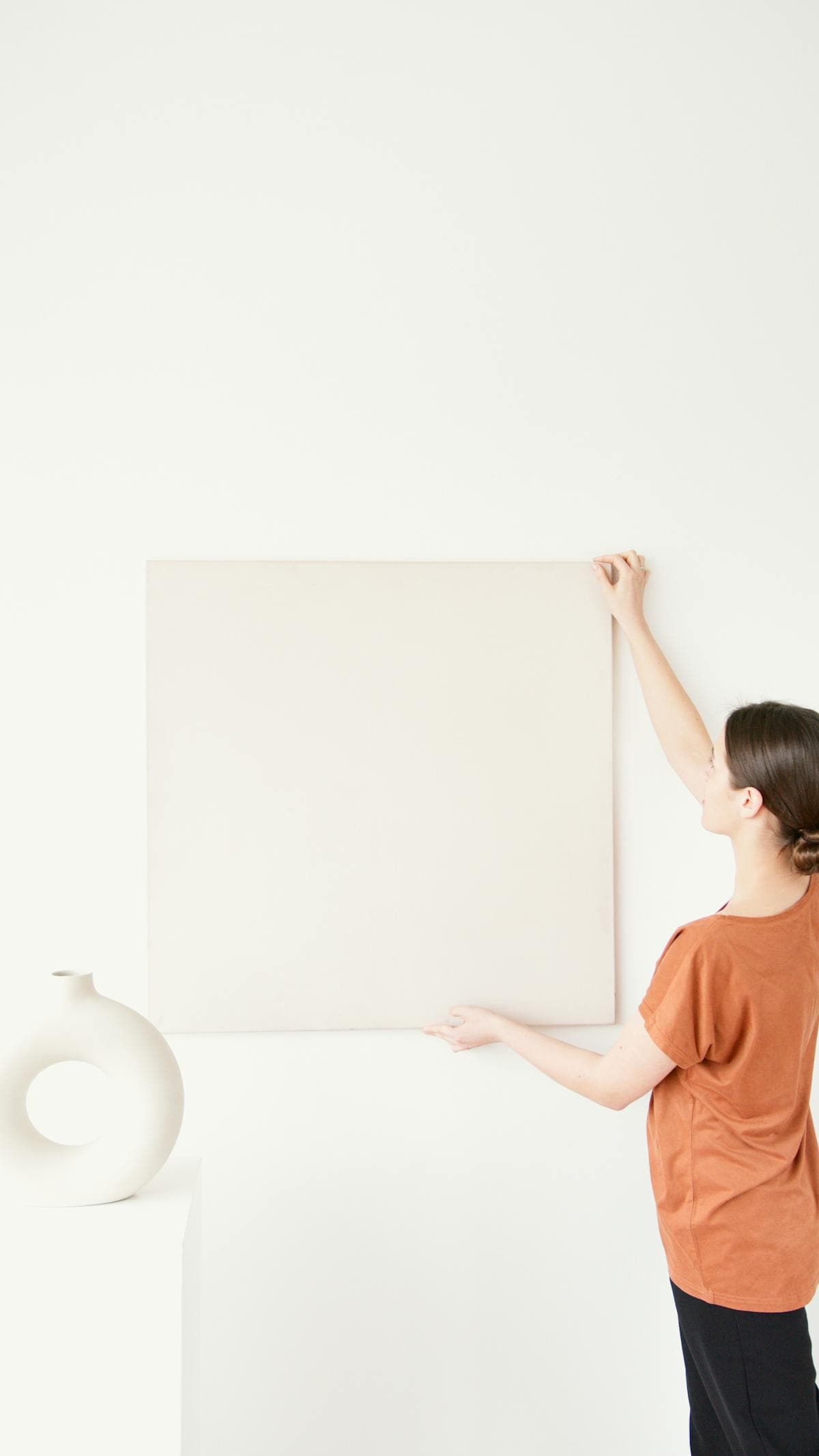 Woman positioning a large canvas on a white wall during an art installation