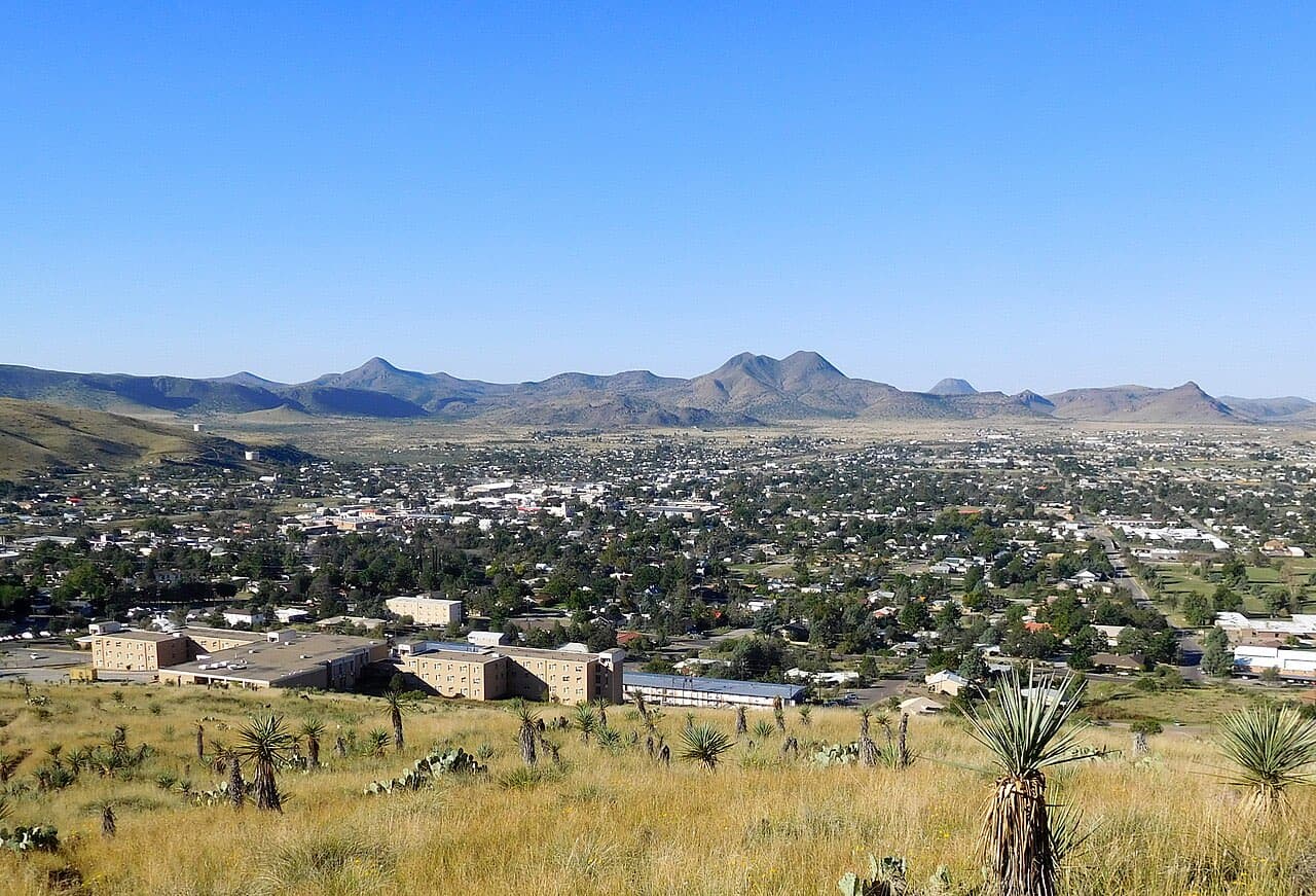 Alpine, Texas spread across its high-desert valley ringed by mountains, seen from the yucca-covered slope of Hancock Hill