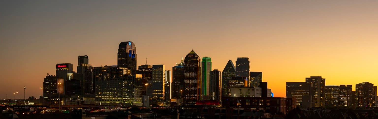 The downtown Dallas skyline glowing at dusk, seen across the Trinity River corridor