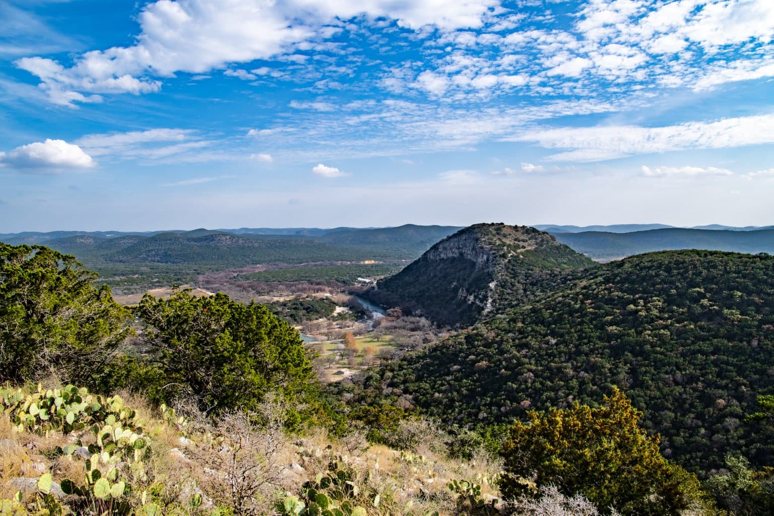 The Frio River valley and Old Baldy's limestone face at Garner State Park, seen from a cactus-dotted overlook under a big Texas sky