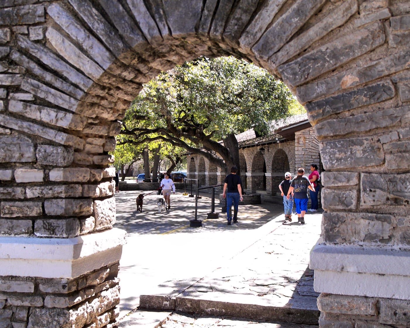 Stone archway of Garner State Park's CCC-built combination building, framing live oaks and the dance terrace beyond
