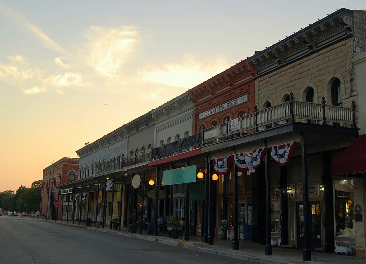 Historic storefronts with iron balconies and patriotic bunting lining Granbury's town square at sunset