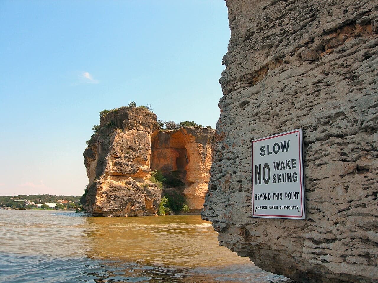 The twin limestone bluffs of Hell's Gate rising from Possum Kingdom Lake, with a no-wake sign posted on the rock face