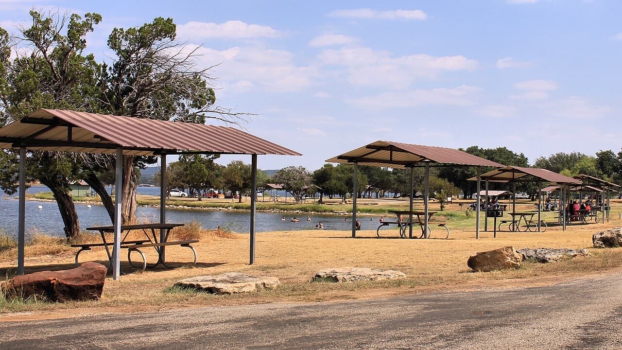 Covered picnic shelters along the swimming cove at Possum Kingdom State Park, with families in the water on a summer day