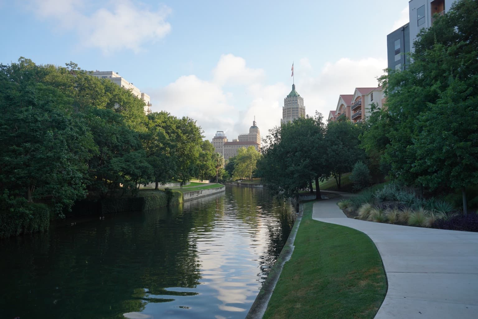 The San Antonio River Walk, with stone footpaths, cypress trees, and restaurants lining both banks of the river