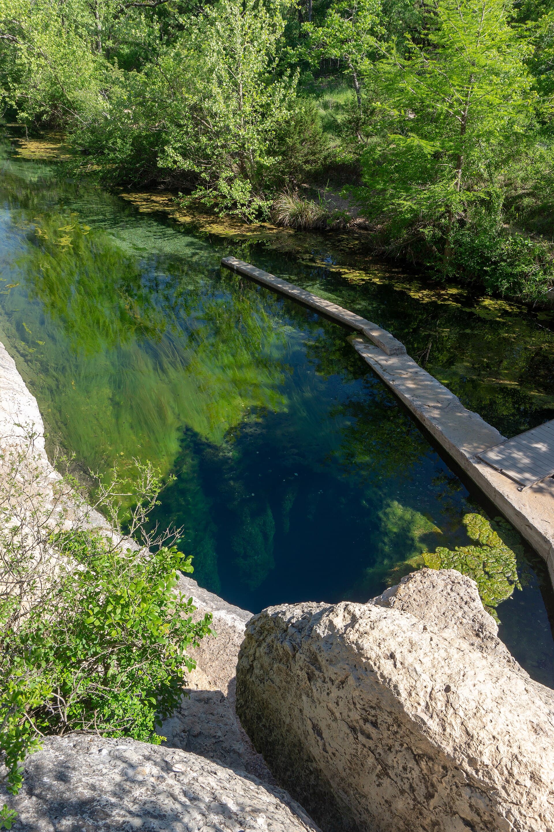 Jacob's Well in Wimberley, Texas — a crystal-clear emerald-green vertical spring opening dropping into a deep underwater cave