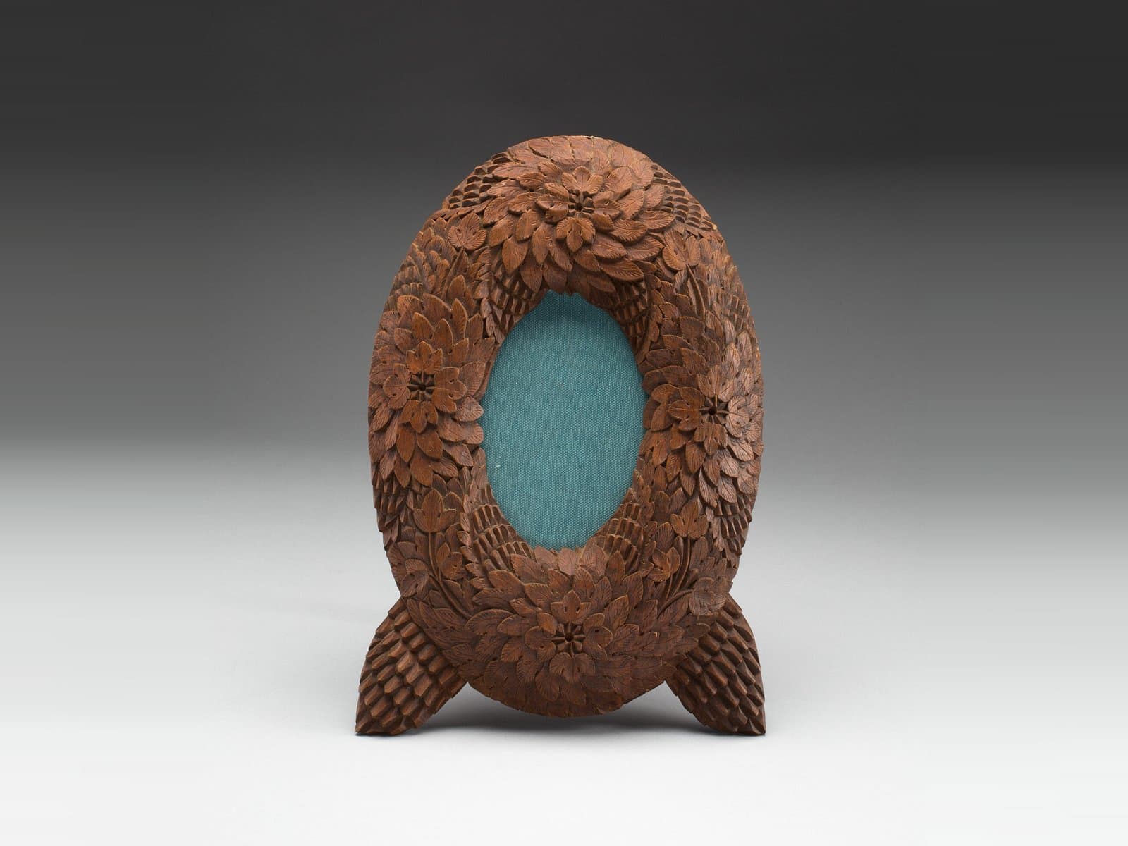 A hand-carved American wooden picture frame with an oval opening, its border carved like overlapping pine cone scales