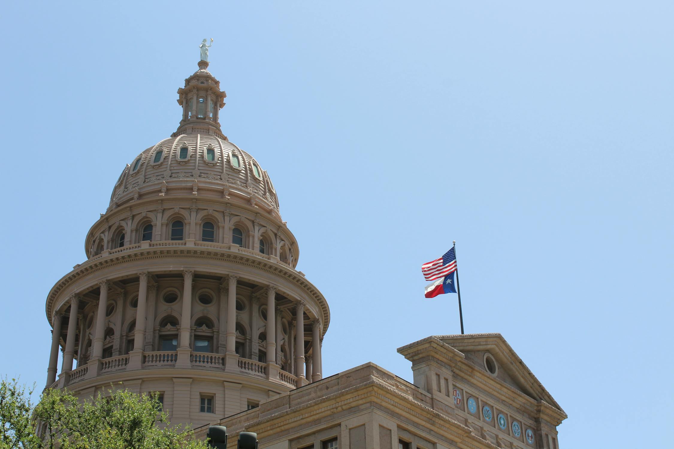 The Texas State Capitol dome with the U.S. and Texas flags — where Governor Abbott froze H-1B petitions and AG Paxton launched fraud investigations