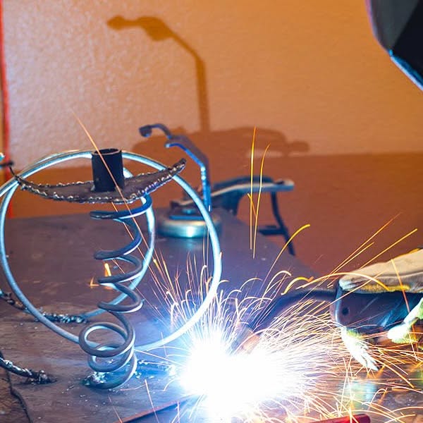 An artist welding a metal sculpture at The Contemporary Austin, sparks flying in the studio
