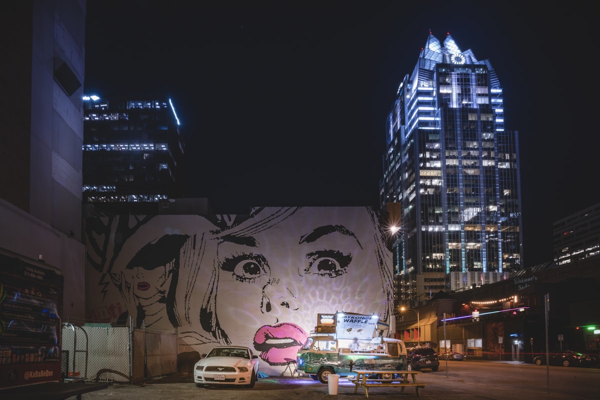 Austin street art mural illuminated at night with the downtown skyline in the background