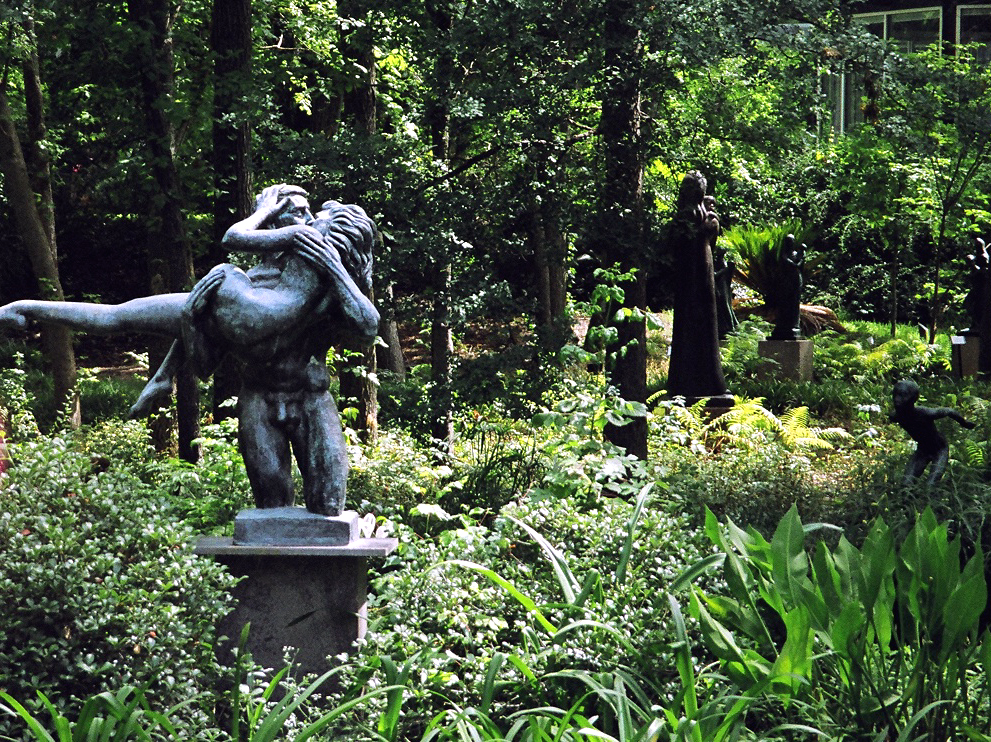 Multiple bronze sculptures along a lush garden path at the UMLAUF Sculpture Garden, shaded by mature trees