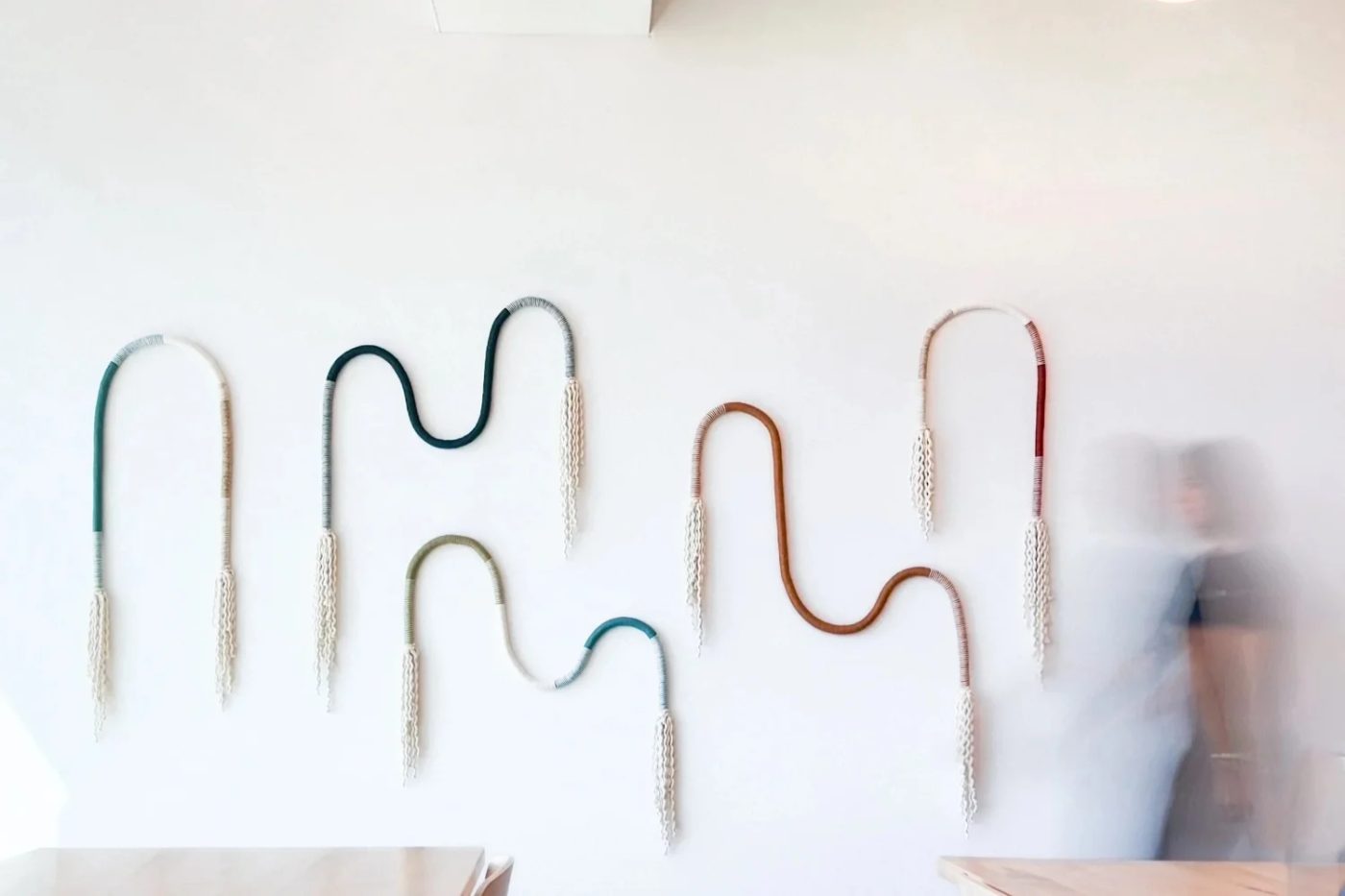 A FIBROUS installation by Ellen Bruxvoort: five sculptural wrapped-rope forms in teal, sage, and rust looping across a white wall