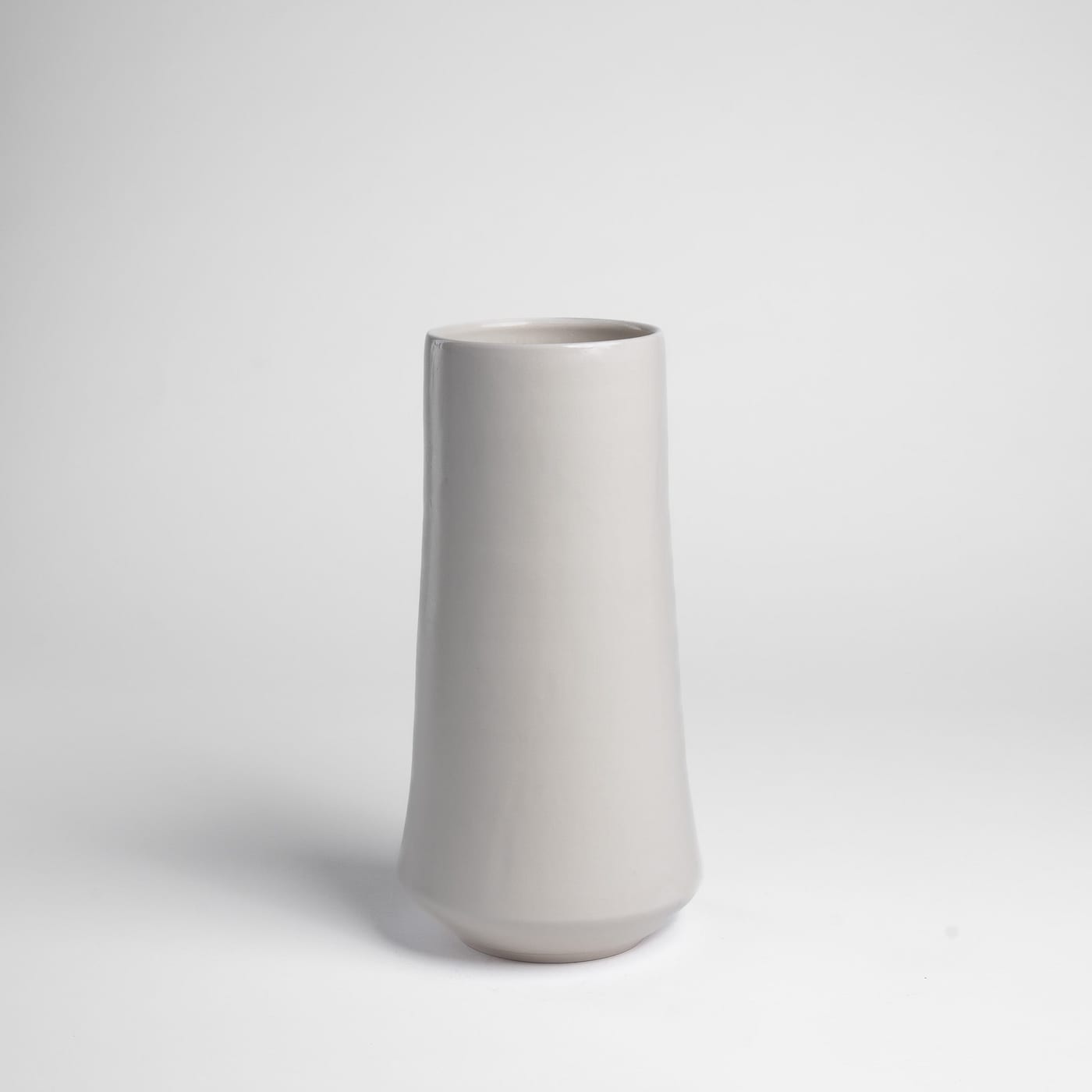 A tapered white high-fired porcelain vase by Keith Kreeger on a plain background